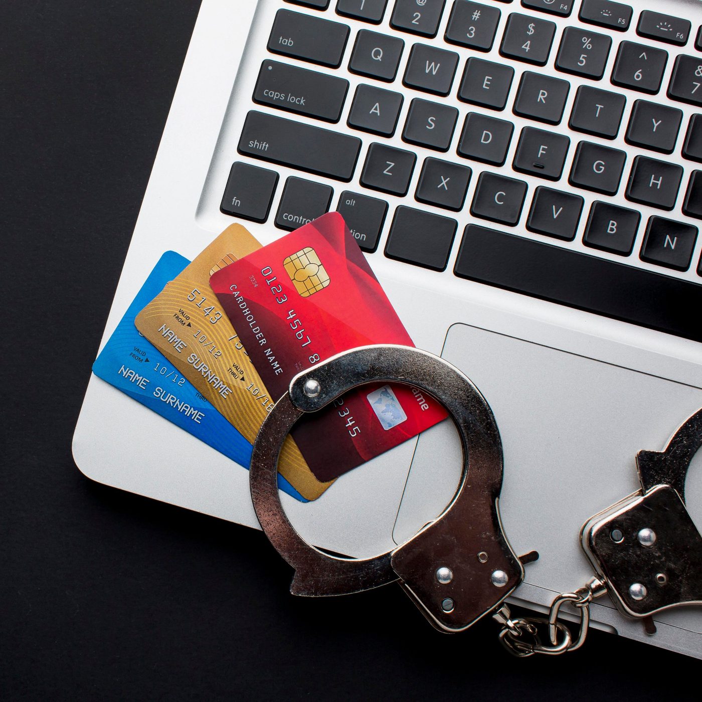 Cartes bancaires et menottes posées sur un ordinateur portable.